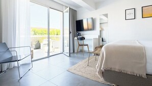 A modern hotel room with a bed, a desk, a chair, a TV, and a sliding glass door to the outside. - Hotel Rhys Denia - Only Adults (Denia)