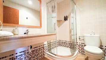 Un baño con ducha envuelta en vidrio, un inodoro y un lavamanos con espejo.
