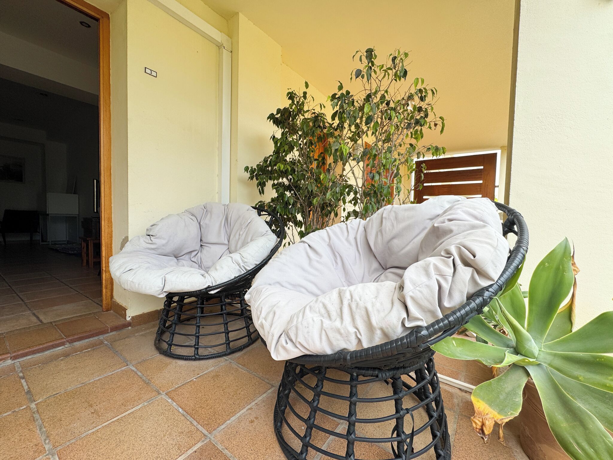 Two wicker chairs with cushions on a tiled patio.