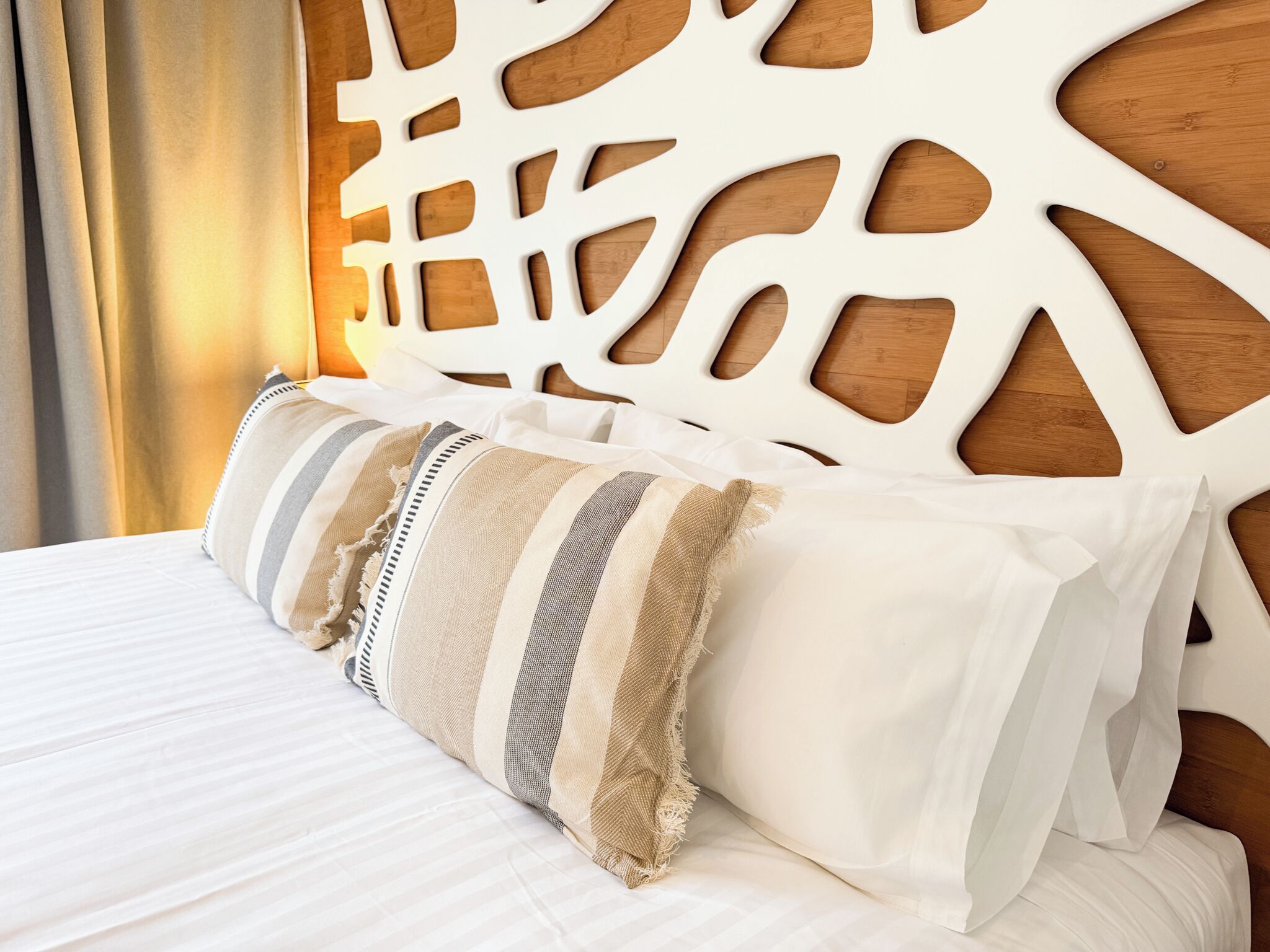 Una cama con ropa blanca y cabecera de madera con diseños recortados.