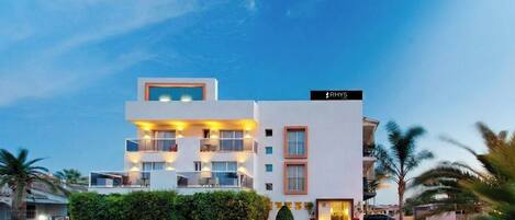 Un hotel moderno con techo plano, varios balcones y un letrero que dice 'RHYS'.