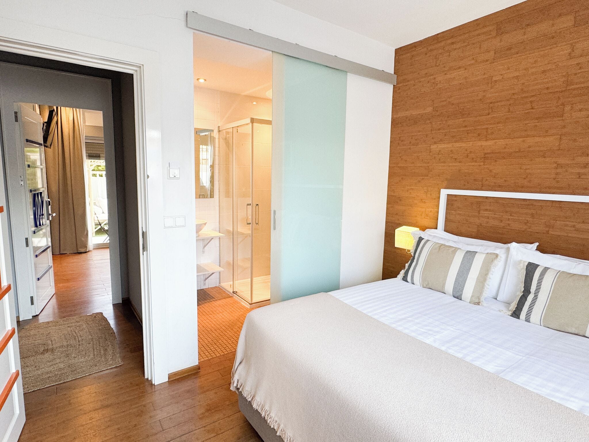 A modern hotel room with a large bed, a wooden headboard, and a glass shower enclosure.