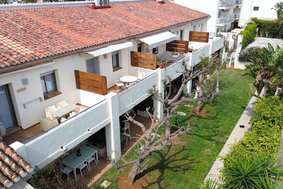 Um edifício de vários andares com telhado em telhas, área de estar ao ar livre e um jardim bem cuidado.