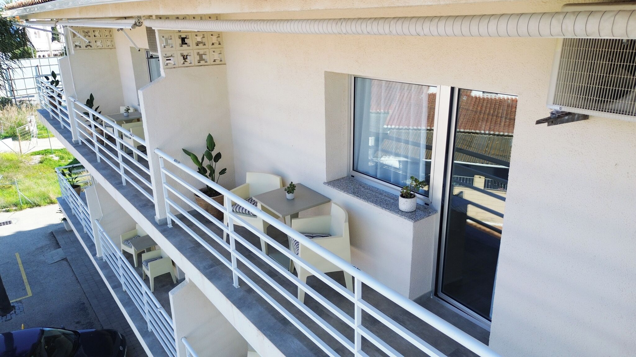 Ein Balkon mit Tisch und Stühlen, Blumentöpfen und einem Fenster mit Blick auf die Straße.