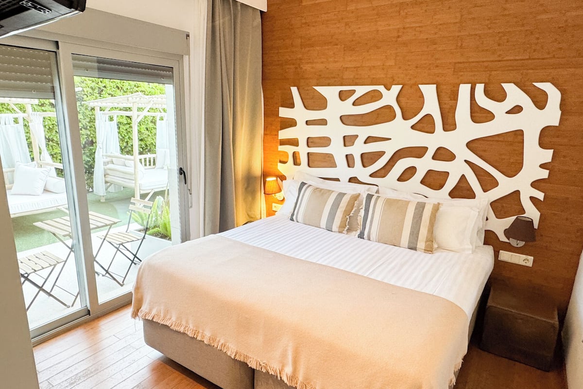 Quarto com cama, cabeceira de madeira, porta de correr de vidro para um pátio e vista para o exterior.