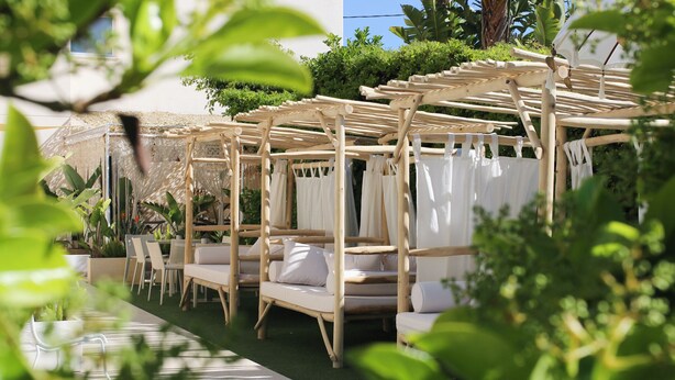 A garden area with wooden pergolas, white cushions, and a pathway. - Hotel Rhys Denia - Only Adults (Denia)