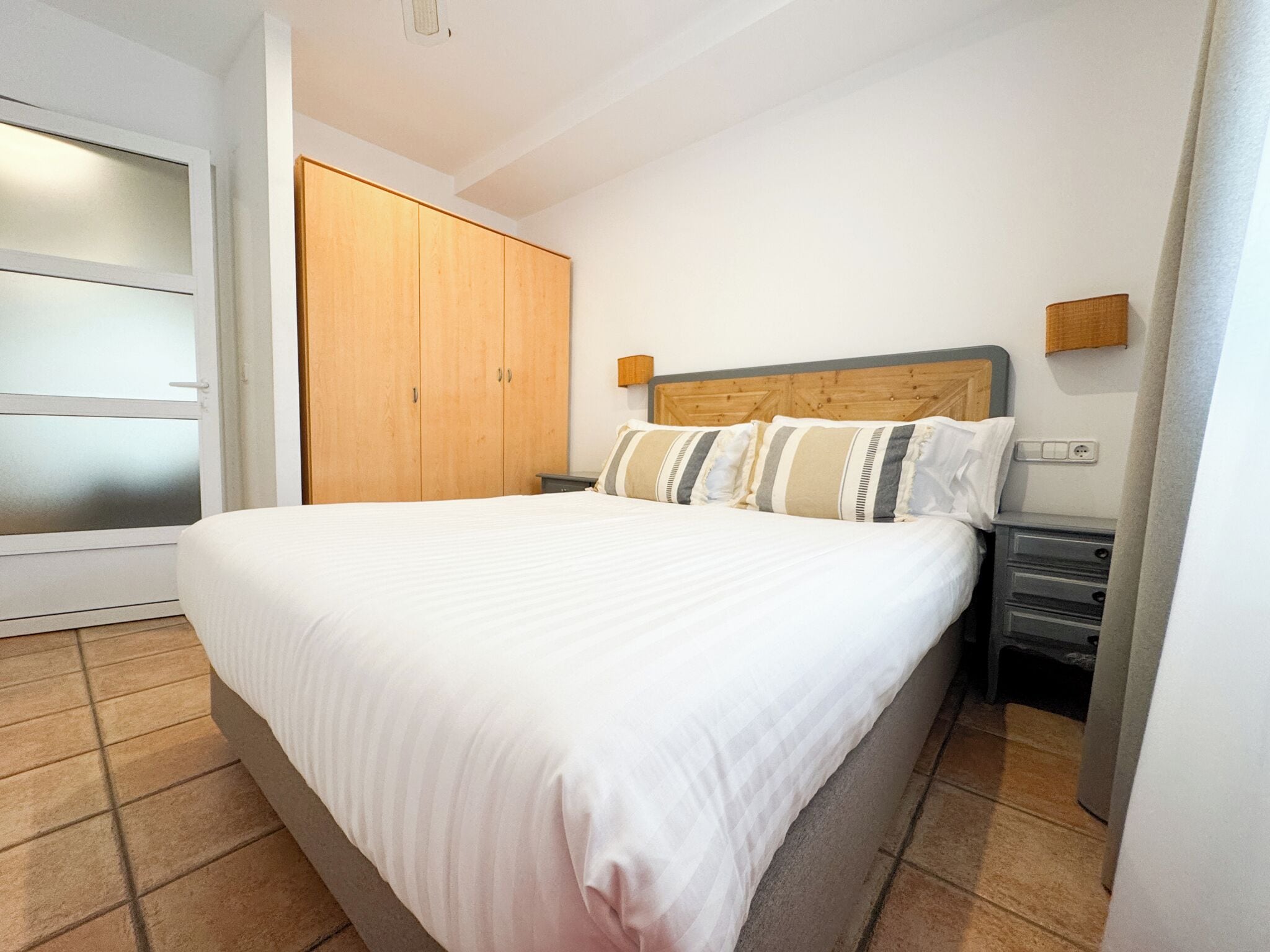 A bedroom with a large bed, wooden wardrobe, and a nightstand.