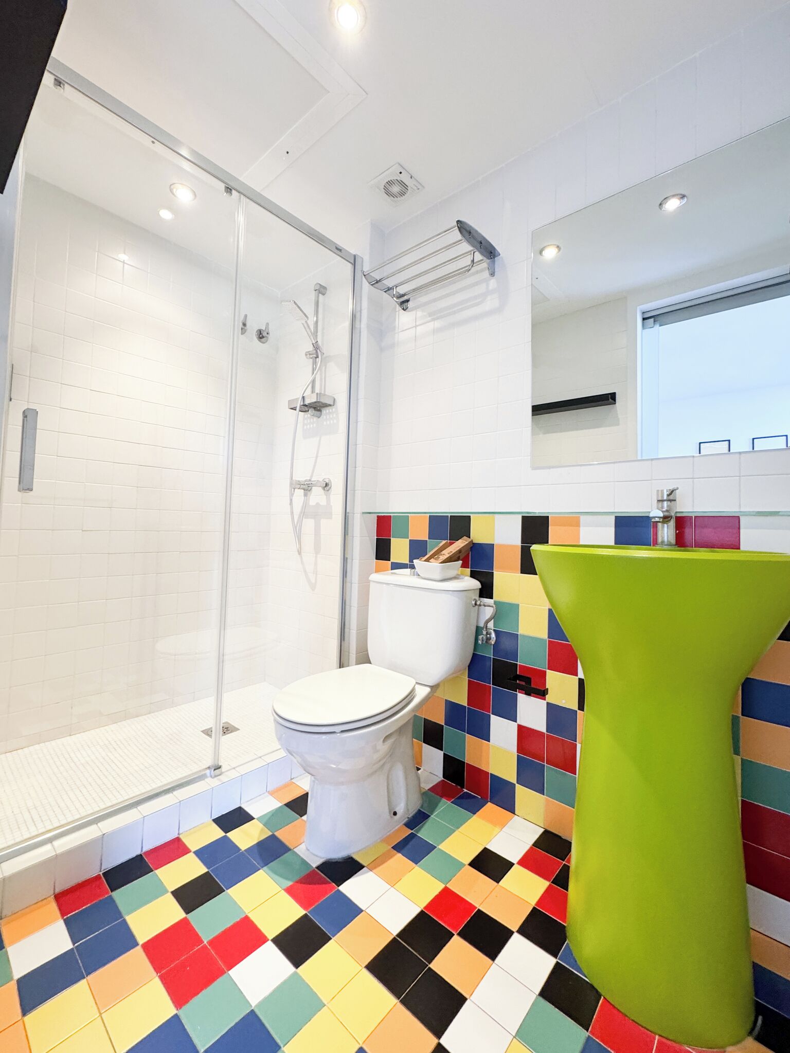 A modern bathroom with a glass shower enclosure, a white toilet, and a colorful tiled floor.