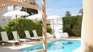 A pool area with white lounge chairs and umbrellas, surrounded by greenery and a white building. - Hotel Rhys Denia - Only Adults (Denia)