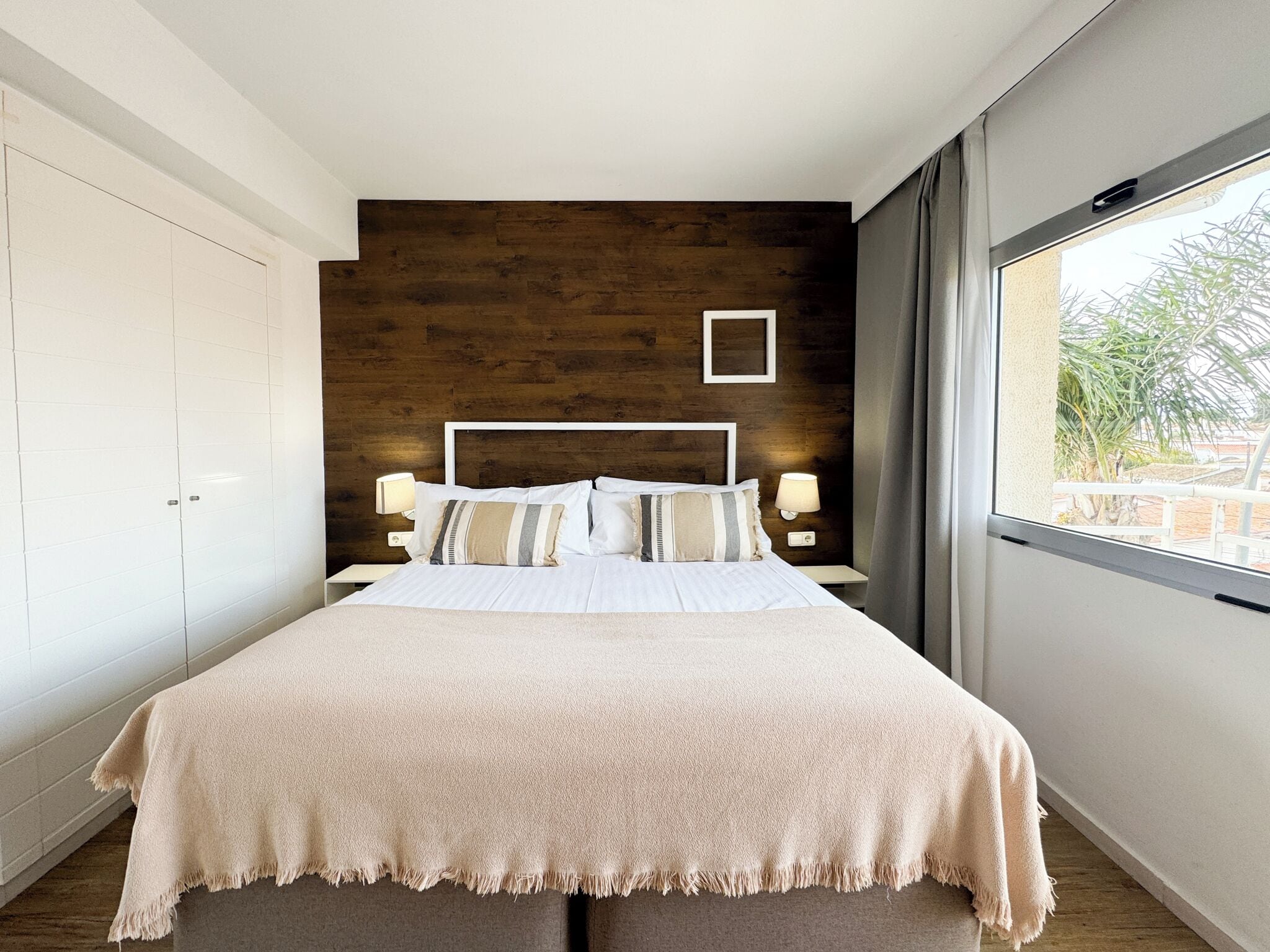 Une chambre moderne avec un grand lit, un mur d’accent en bois et une fenêtre donnant sur un paysage verdoyant.