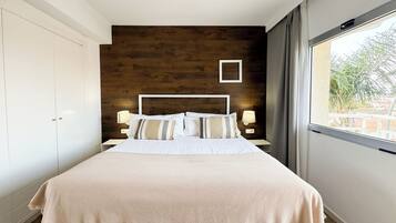 Une chambre moderne avec un grand lit, un mur d’accent en bois et une fenêtre donnant sur un paysage verdoyant.