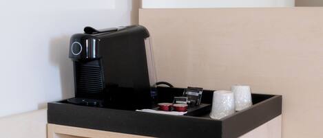 A coffee machine, a small container, and two cups on a counter.