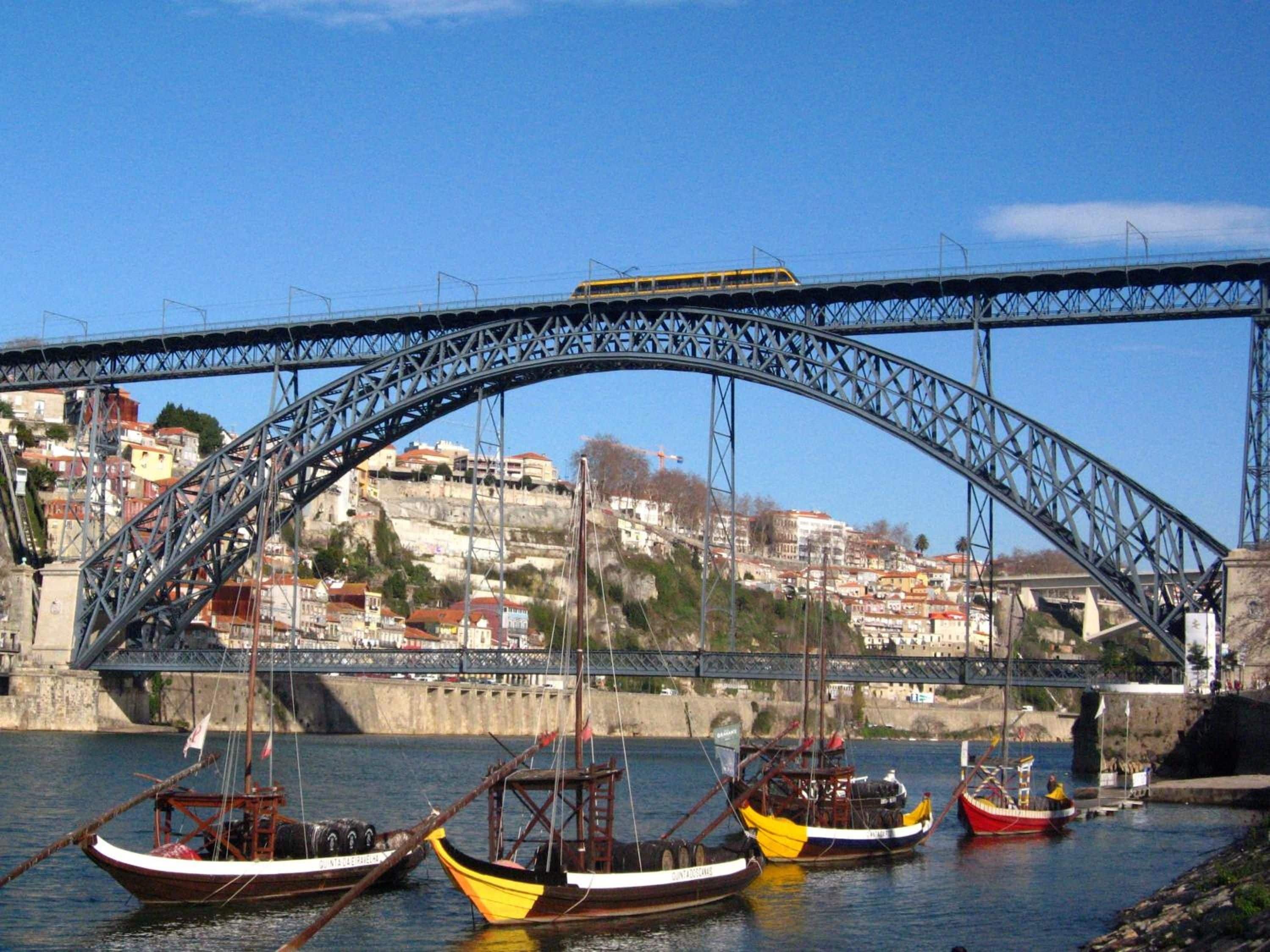Uma ponte com um trem amarelo, barcos na água e edifícios ao fundo.