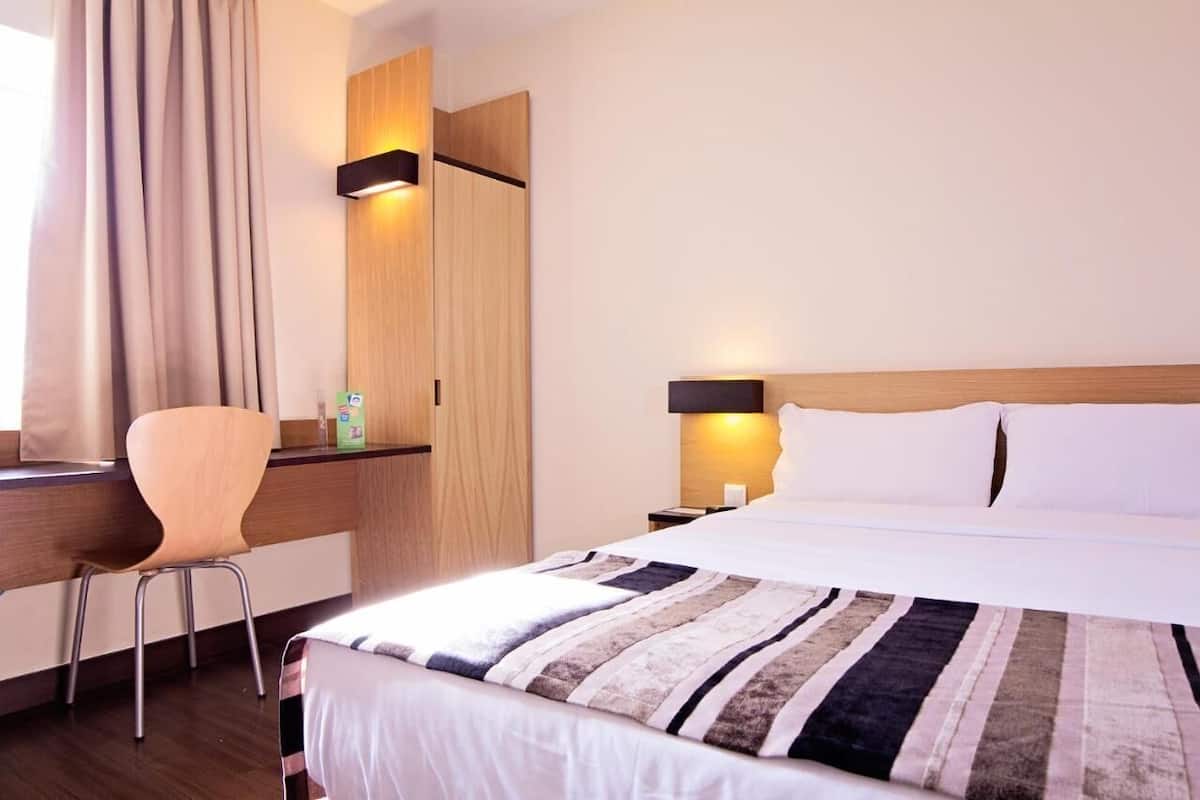 A hotel room with a bed, a desk, a chair, and a wardrobe.