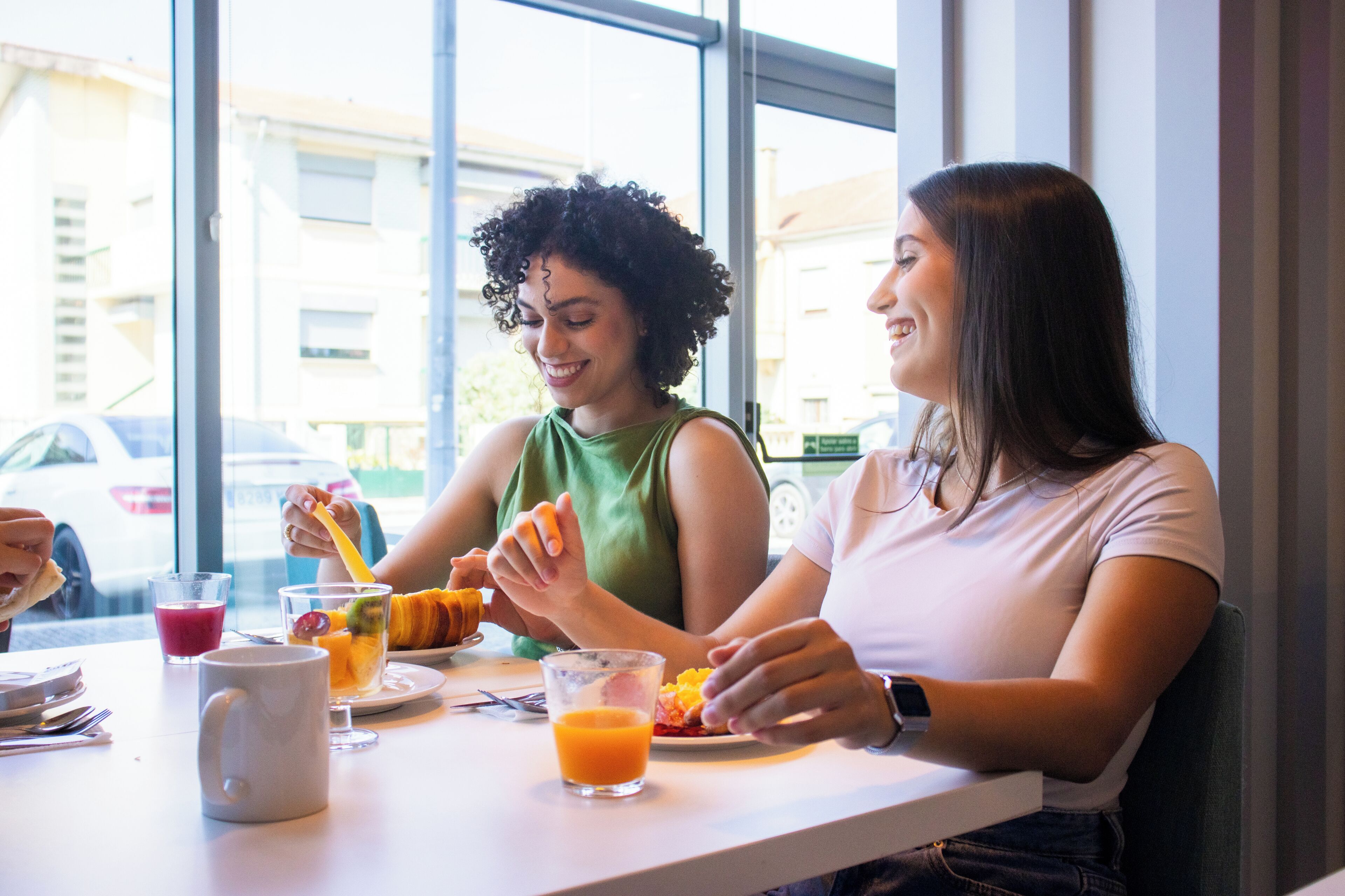 Dos personas cenando en una mesa con vistas a la ventana, un vaso de zumo de naranja y una taza blanca.