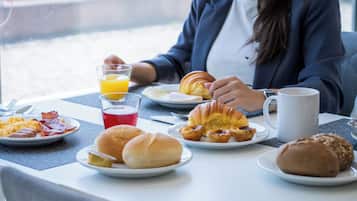 Taula de l'esmorzar amb plats de menjar, un got de suc d'aranja i una tassa de cafè.