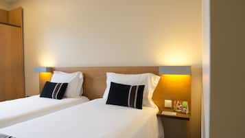 Habitación de hotel con dos camas, cada una con ropa blanca y almohadas negras, cabecero de madera y mesitas de noche con lámparas y tarjetas informativas.