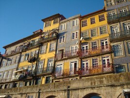Una hilera de edificios coloridos con balcones, algunos con ropa tendida, y un arco de piedra al frente.