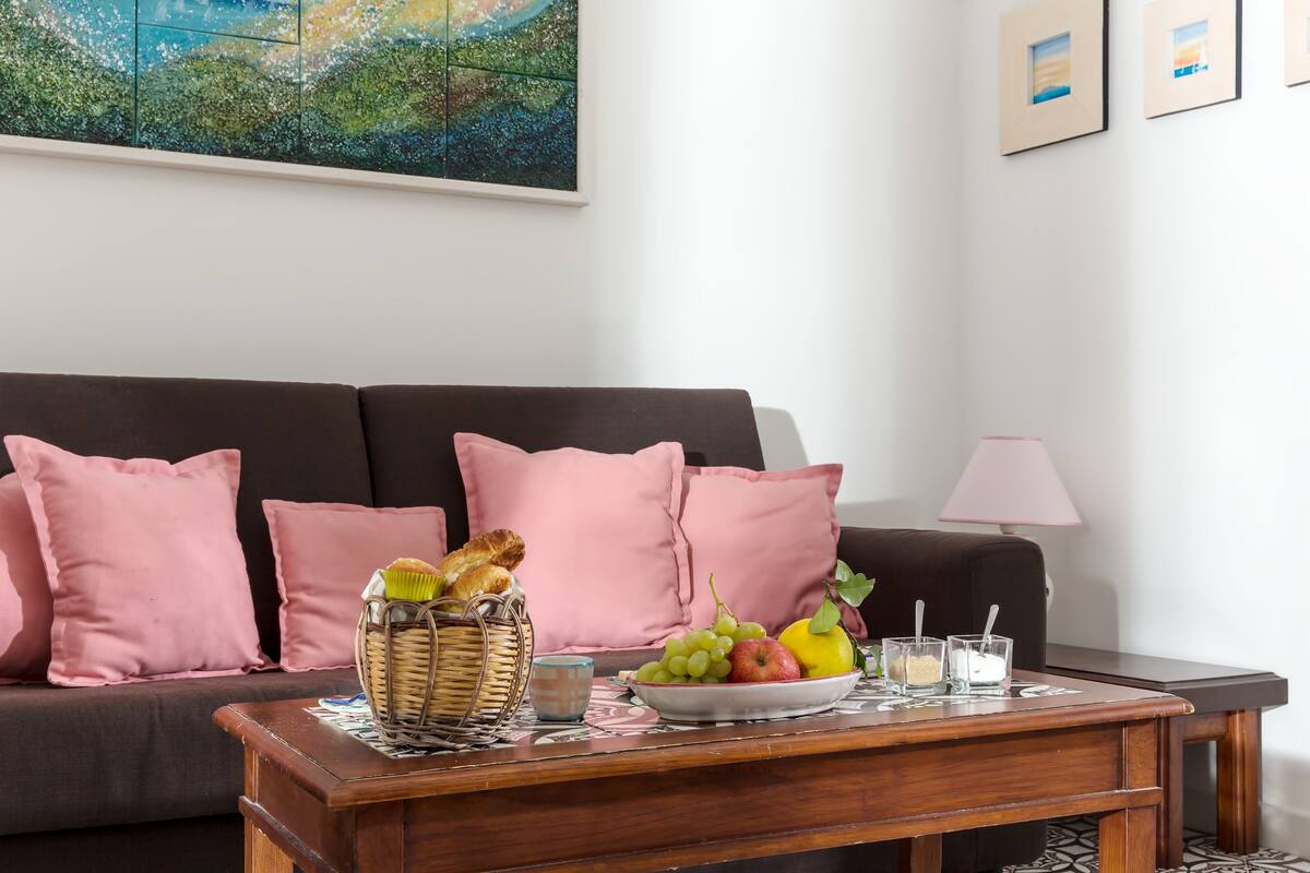 Un salon avec un canapé, une table basse sur laquelle se trouvent des fruits et un panier, et une lampe.