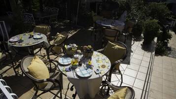 Een terras buiten met ronde tafels en stoelen, omringd door potplanten en een betegelde vloer.