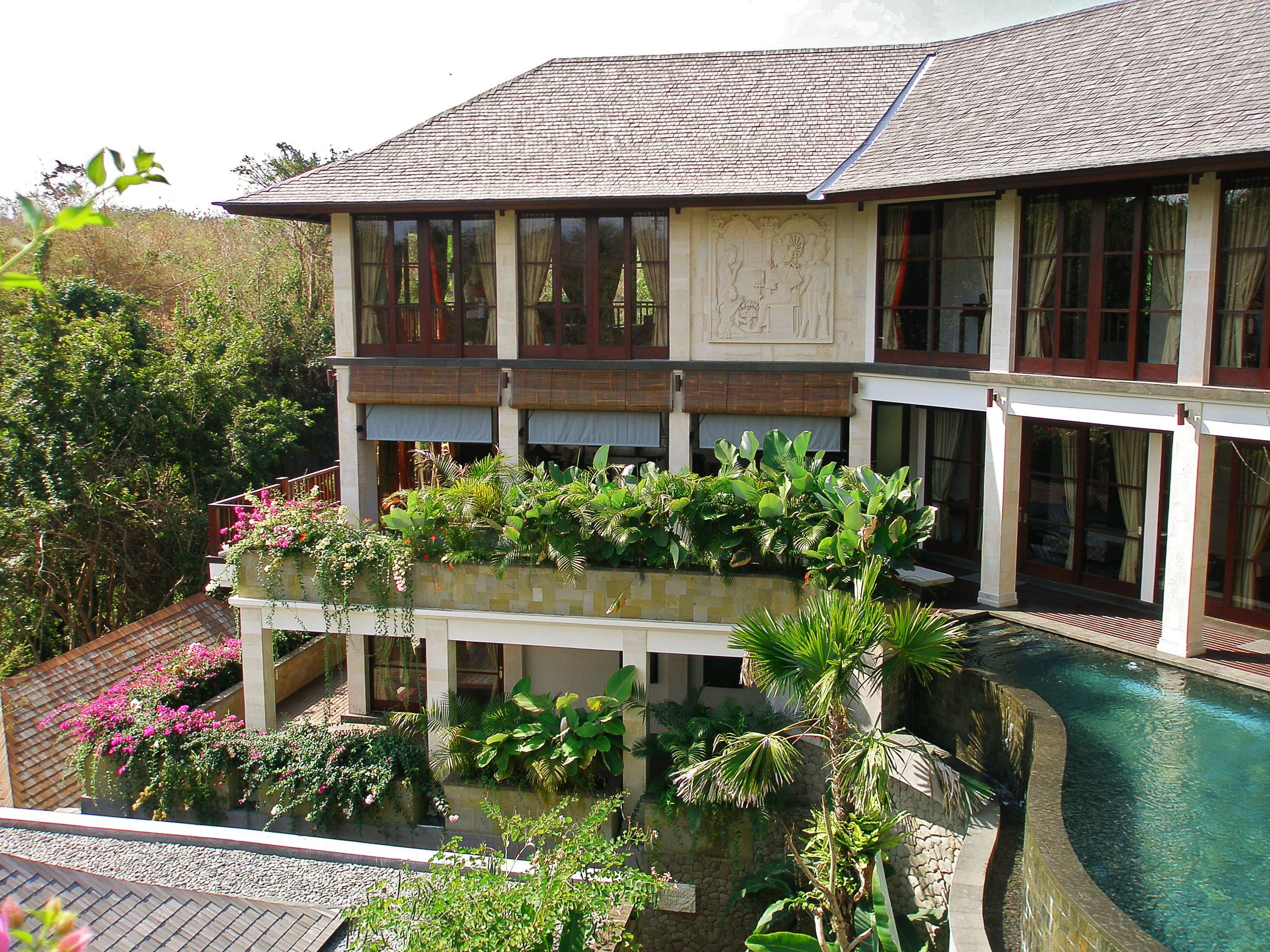 A two-story building with a swimming pool, surrounded by lush greenery and tropical plants.