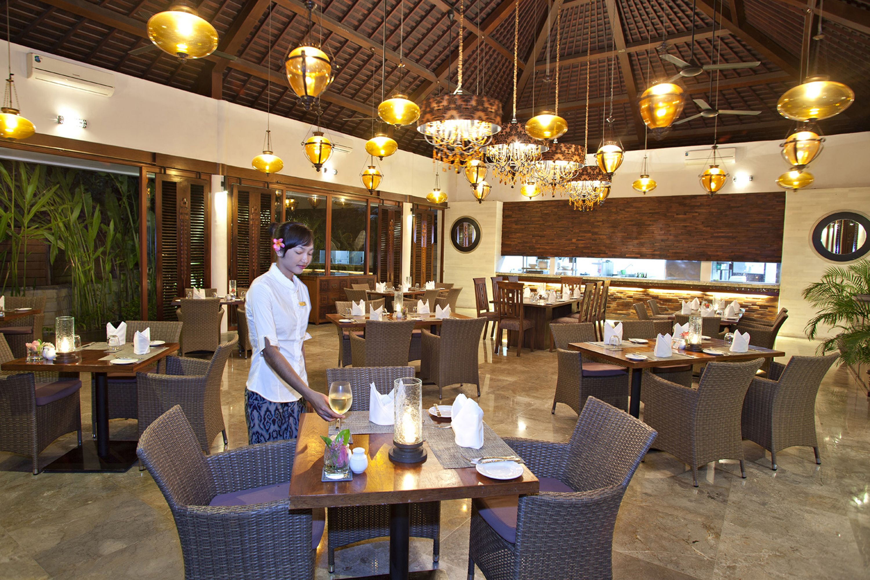 A restaurant with wicker furniture, wooden tables, and hanging chandeliers.