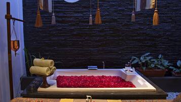 Un cuarto de spa con una bañera llena de pétalos de rosa, un perchero y una camilla de masaje.