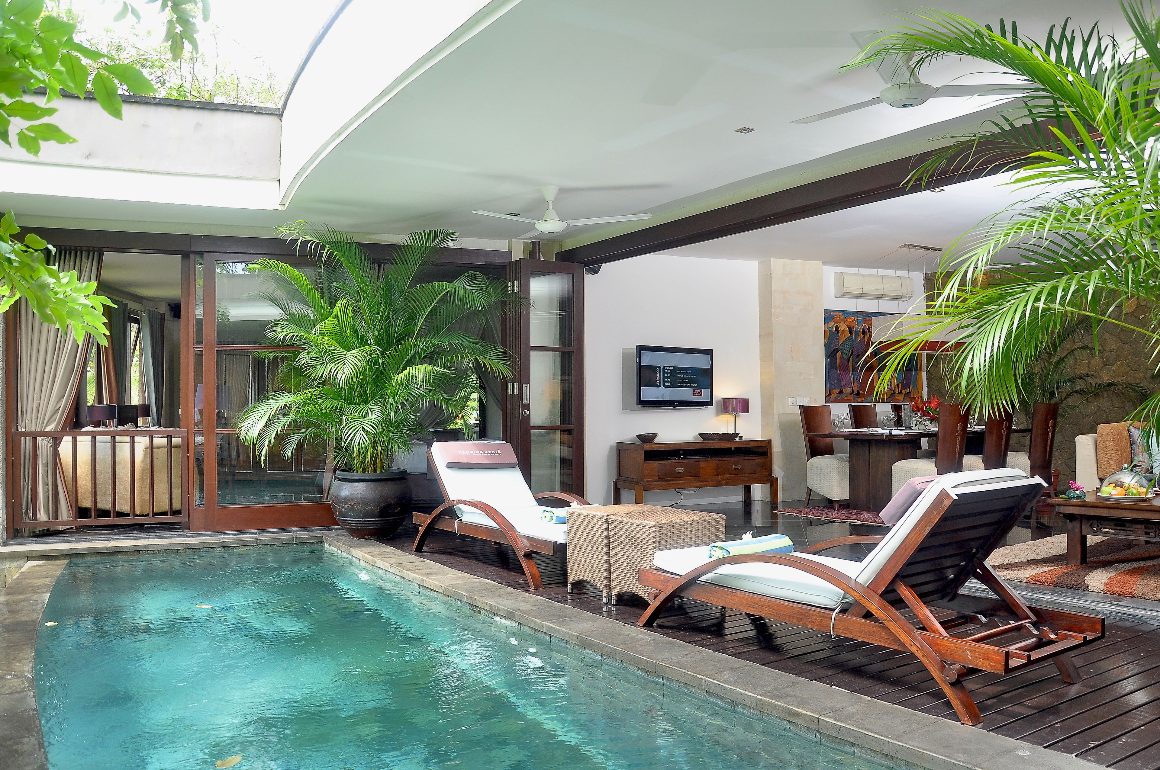 A poolside area with lounge chairs, a dining table, and a ceiling fan.