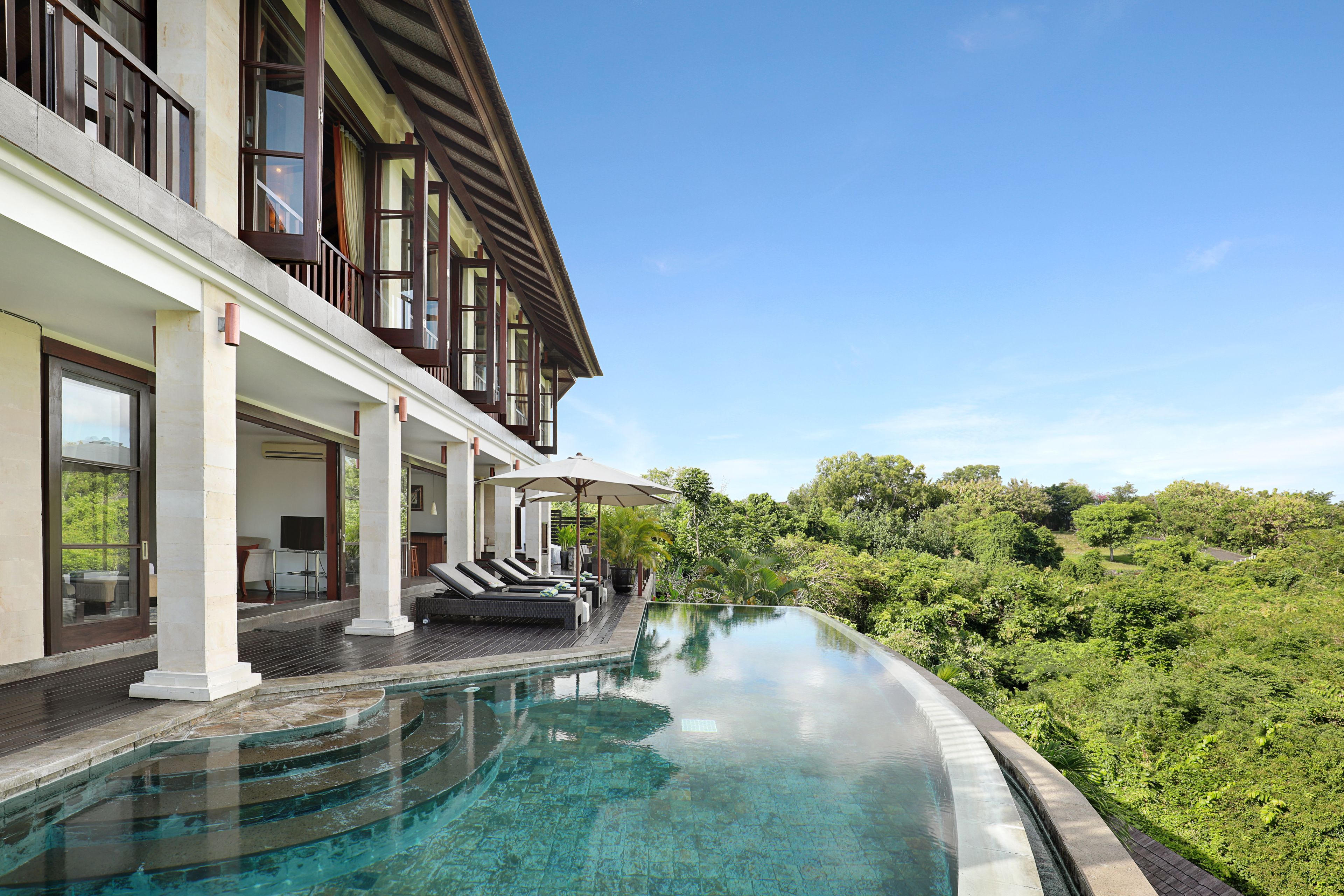 A modern hotel with a large infinity pool overlooking lush greenery.