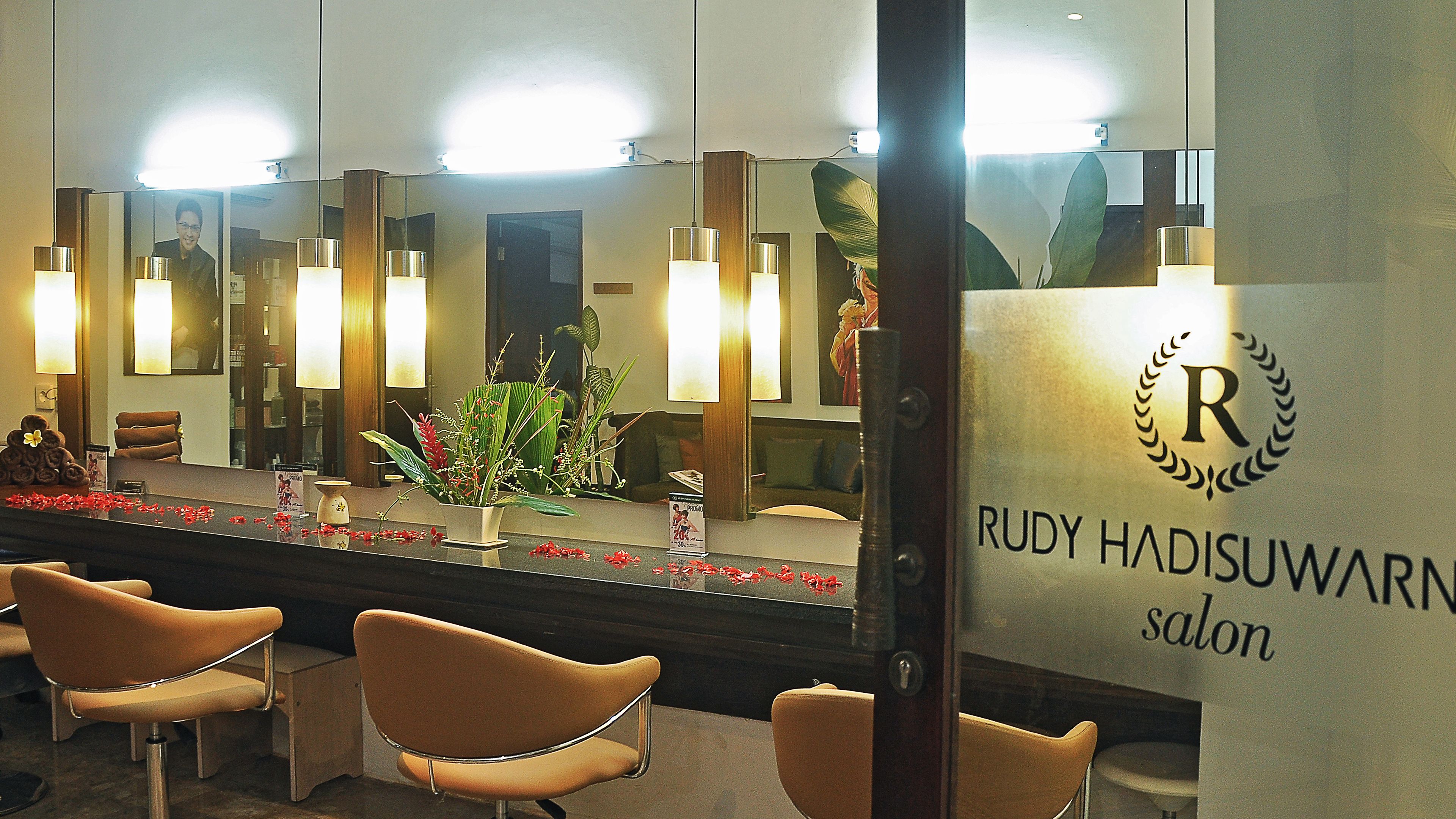A salon interior with a reception desk, seating area, and a large mirror reflecting the space.