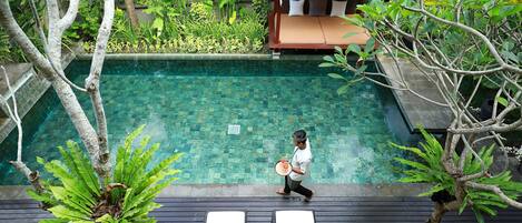 A pool area with lounge chairs, a person walking with a tray, and lush greenery.