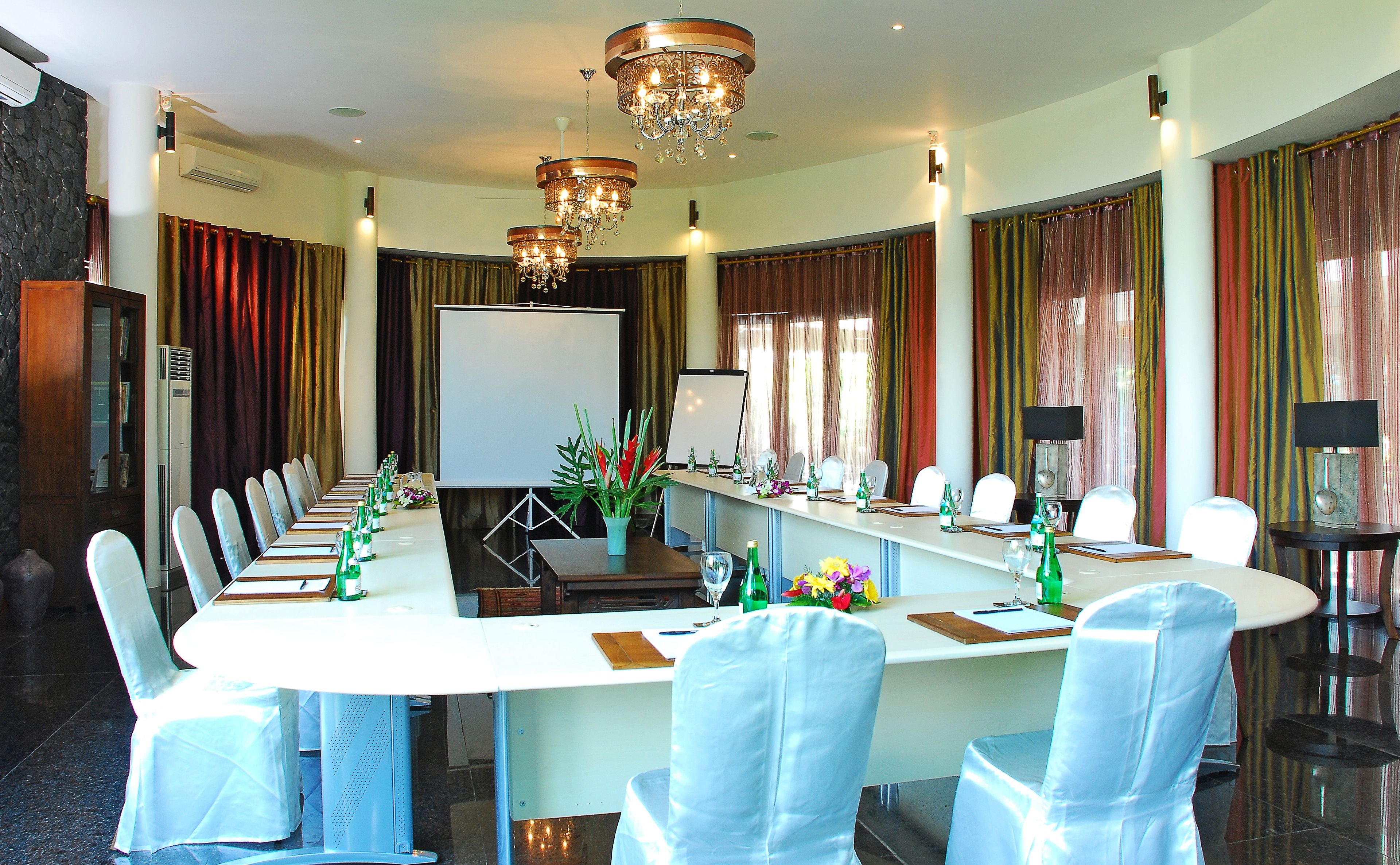 A conference room with a long table, chairs, a projector screen, and a chandelier.
