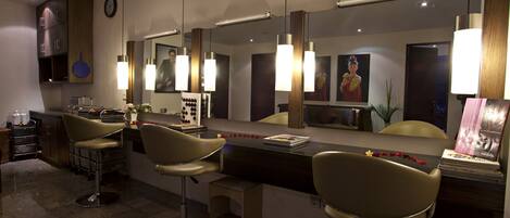 A modern bar area with three bar stools, a counter with a mirror, and pendant lighting.