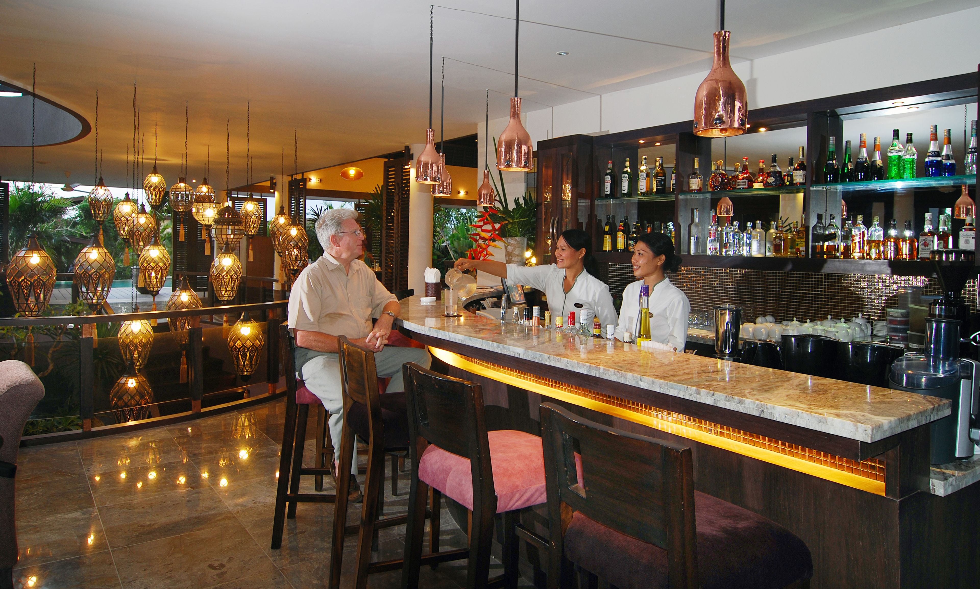 A bar area with a marble countertop, hanging copper pendant lights, and a variety of liquor bottles.