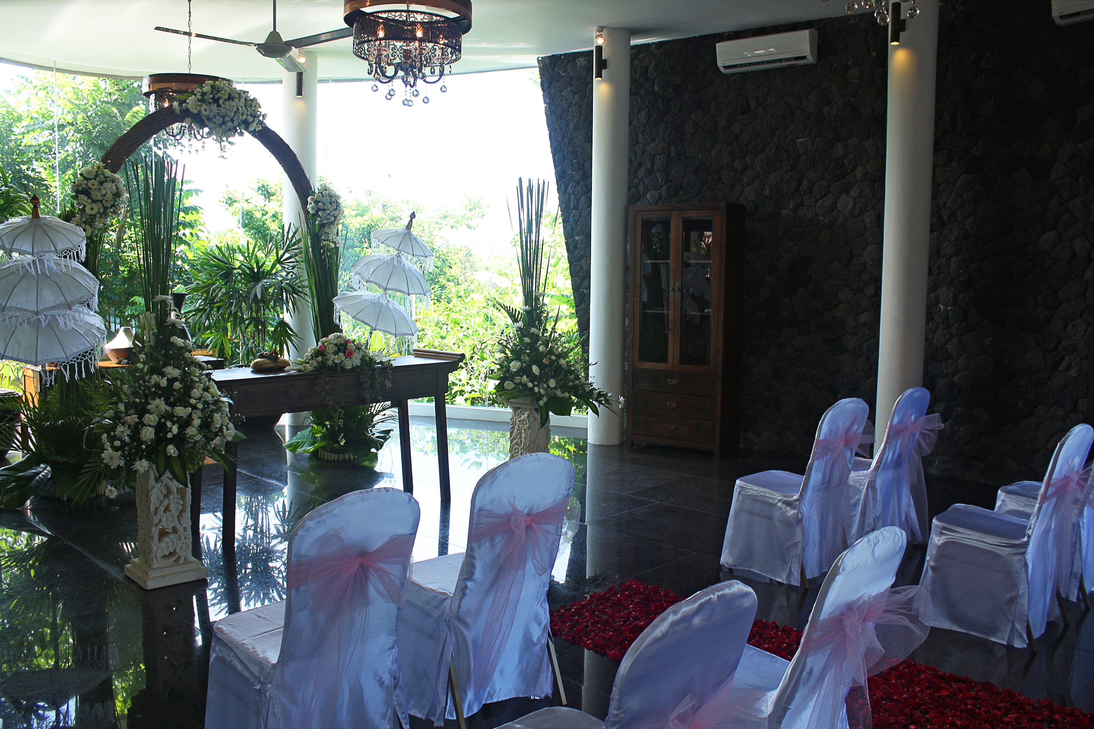 A wedding venue with white chairs, floral decorations, and a stone wall.