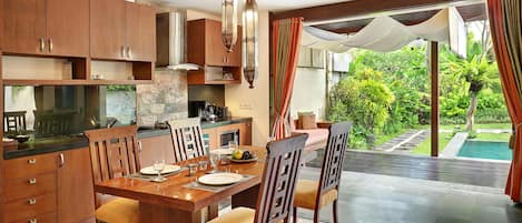 A modern kitchen with wooden cabinets, a dining table set for four, and a view of a swimming pool.