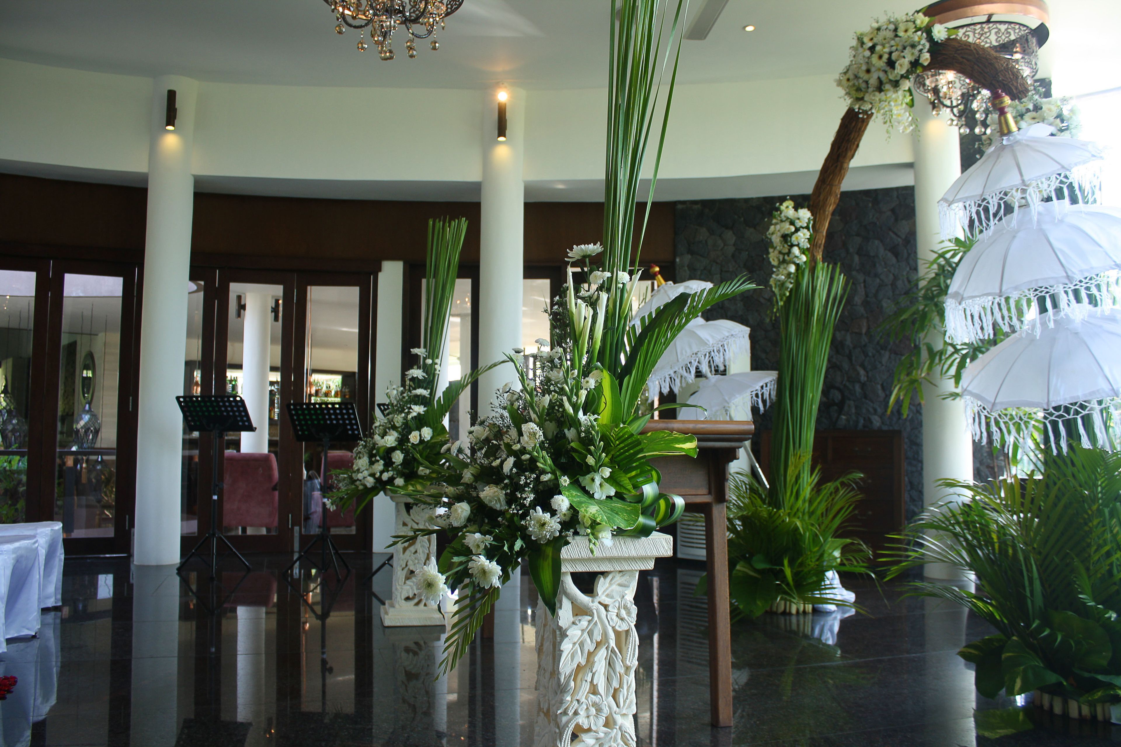 Un vestíbulo con piso pulido, una mesa de recepción y una columna blanca decorada con un arreglo floral.
