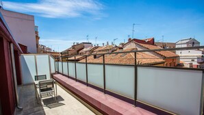 Un balcón con barandilla de vidrio, una silla y vistas a edificios con tejados de teja.