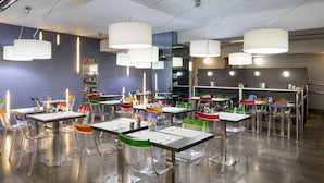 Un restaurante moderno con sillas traslúcidas, mesas blancas e iluminación colgante.