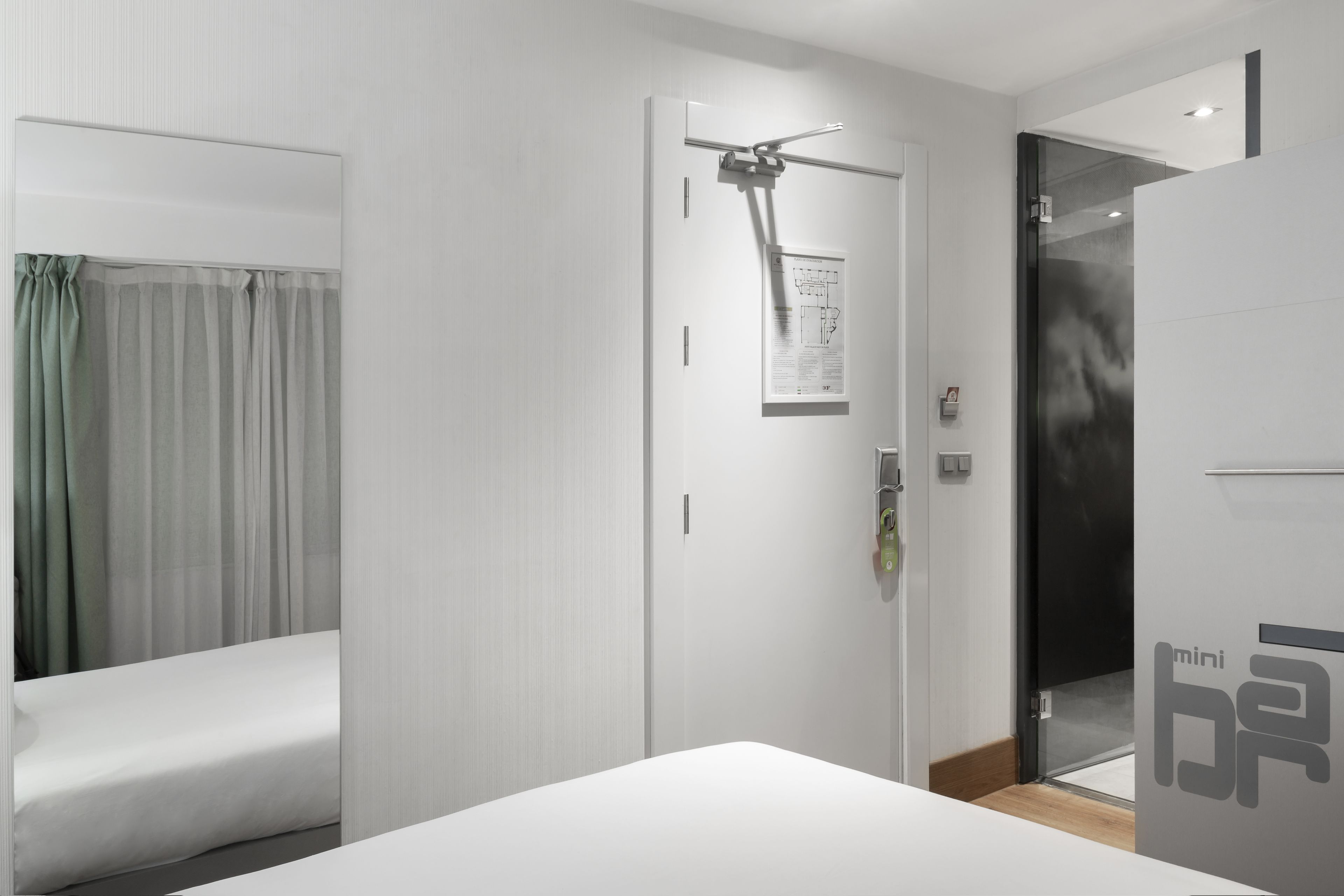 Una habitación de hotel moderna con una cama, una puerta con cámara de seguridad y un separador de vidrio.