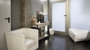 Un baño moderno con una bañera blanca, un inodoro blanco y un lavabo blanco con espejo. Hay un estante pequeño con libros y un recipiente de vidrio. Las paredes tienen una textura y hay una ventana con vistas al exterior.
