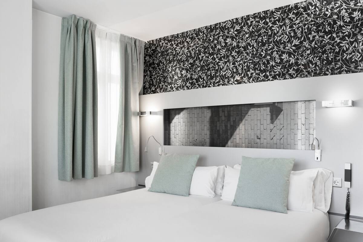 Habitación de hotel moderna con una cama grande, cabecera con diseño de ladrillo, luz de pared y toma de corriente.