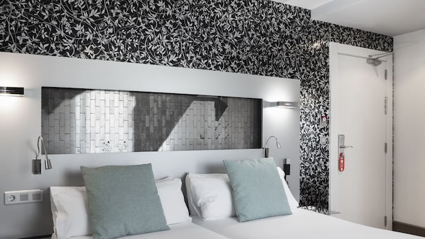 Una habitación de hotel moderna con una pared de ladrillo, un espejo grande y una cama con dos almohadas.