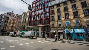 Vista de la calle con edificios, un paso de cebra y algunas personas caminando.