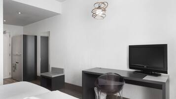 A modern hotel room with a bed, a desk with a TV, a chair, and a unique pendant light.