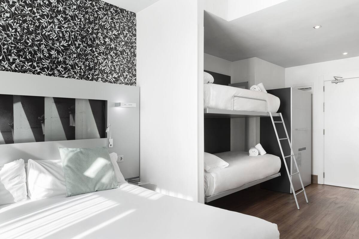 Una habitación de hotel moderna con una cama litera, una escalera y un tocador en la pared.