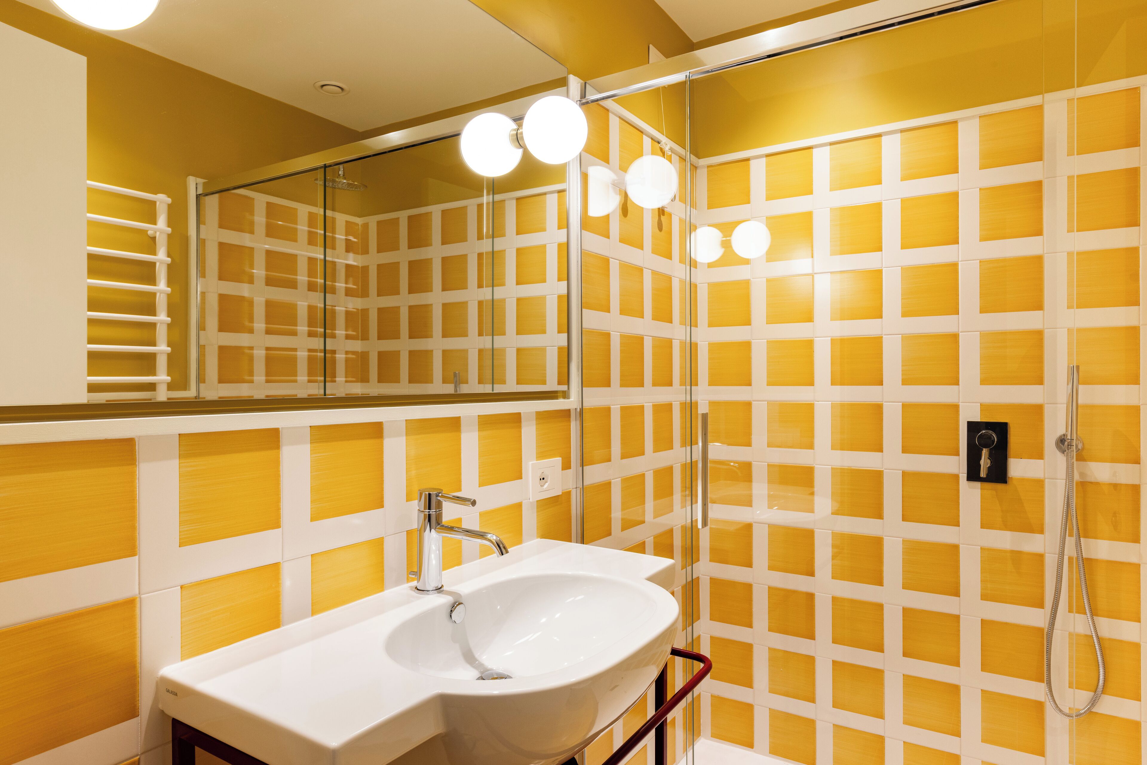 Un baño con lavamanos blanco, un espejo y una ducha con puerta de vidrio.