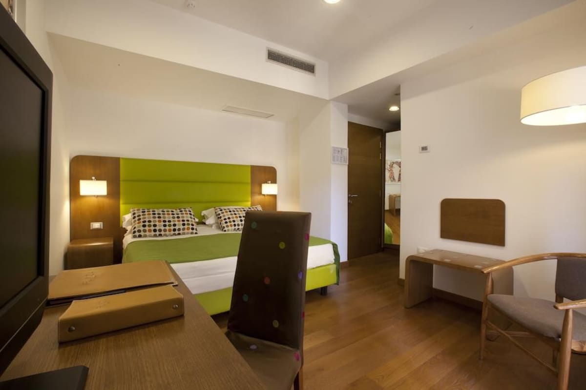 A hotel room with a bed, a desk, a chair, and a television.