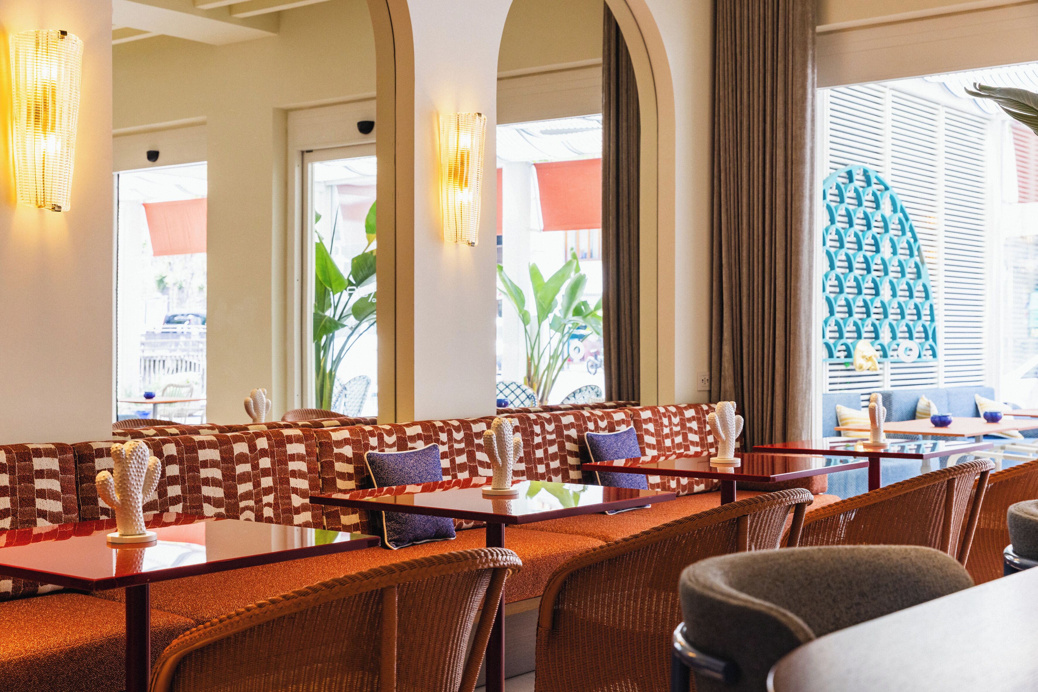 A restaurant with high tables and cushioned booths, large windows with curtains, and decorative wall sconces.