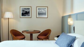 Habitación de hotel con una cama, dos sillones de mimbre, una mesita redonda y dos cuadros en la pared.